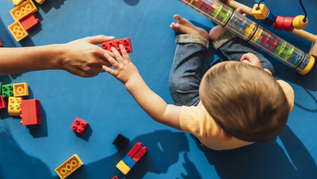 Happy baby playing with toy blocks in the kindergarten.