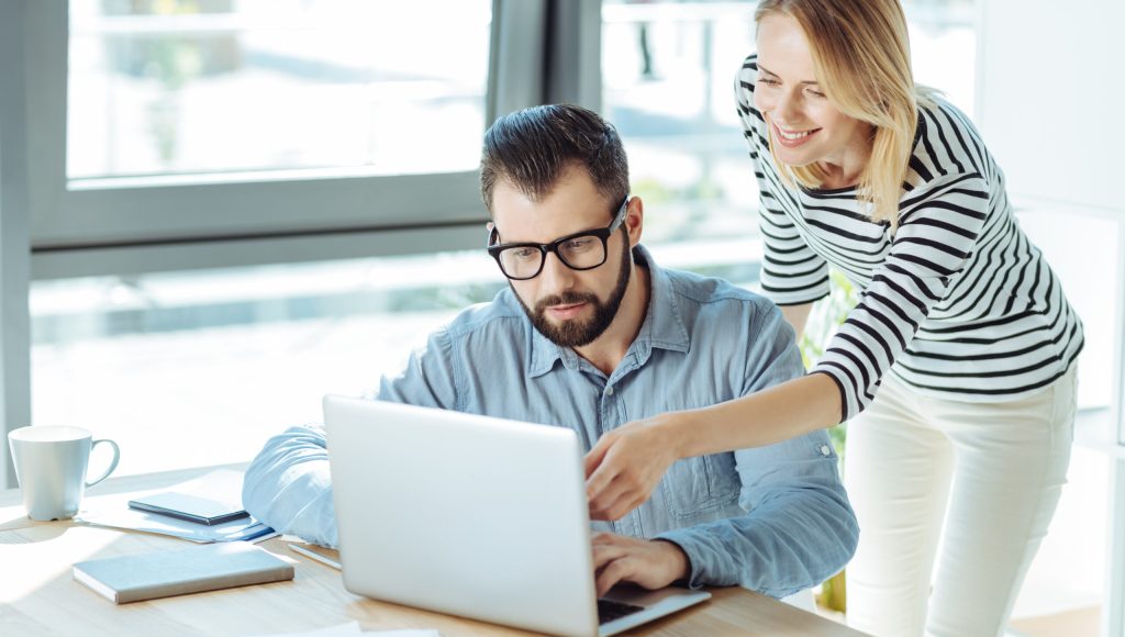 Helpful advice. Charming young woman pointing at the laptop screen and suggesting new idea to her male colleague working on a new company project