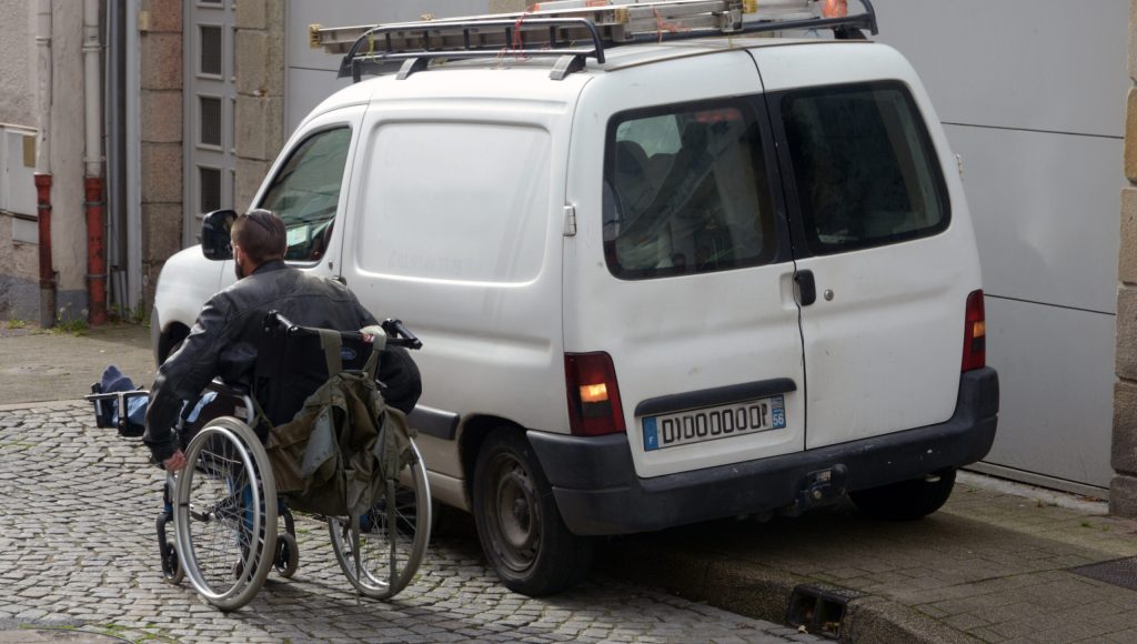 Personne en fauteuil roulant obligée de passer sur la route à