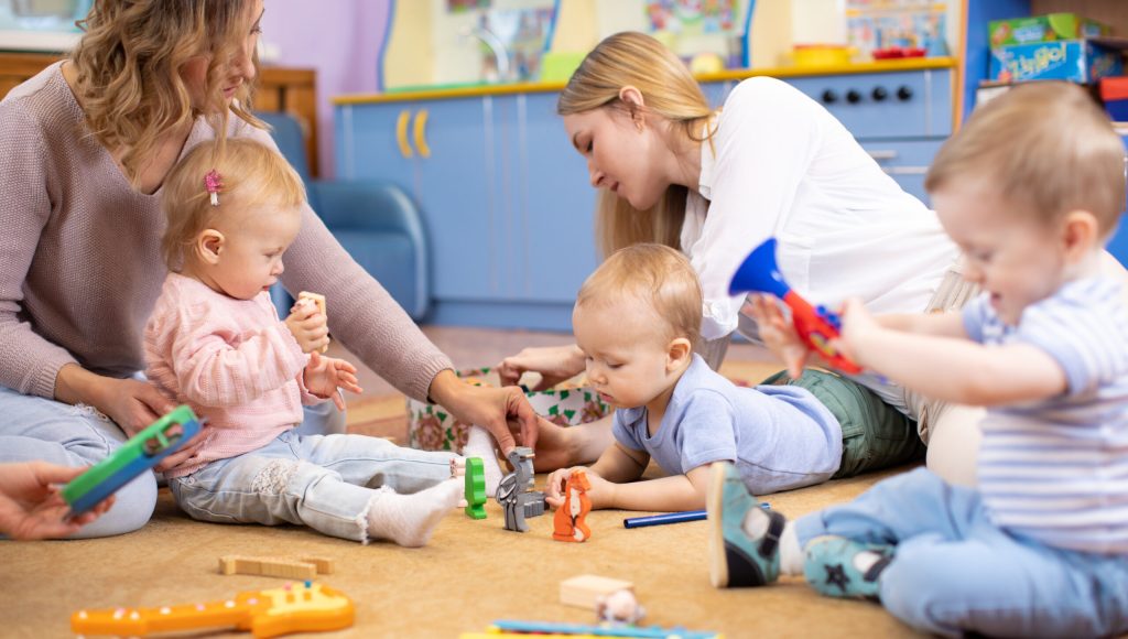 Friends with children toddlers playing on the floor in montessori centre