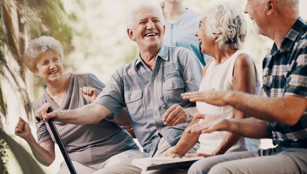 Happy elderly man with walking stick and smiling senior people relaxing in the garden