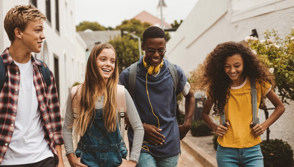 Group of multiethnic college friends walking in the street. Smiling teenage friends wearing college bags walking outdoors and talking.