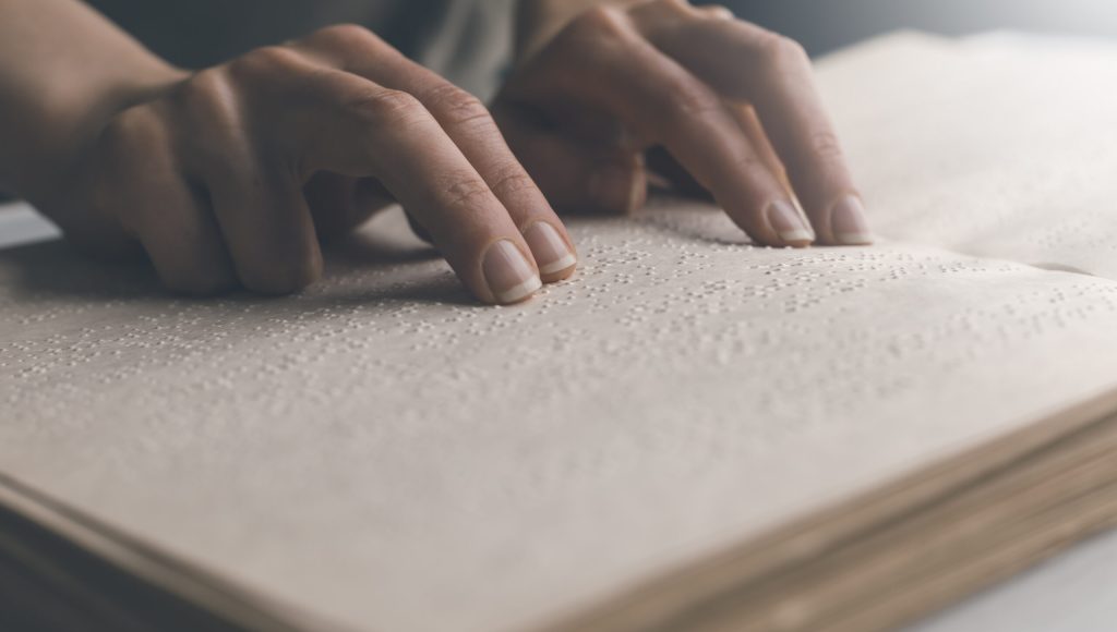 The hand of a blind man reads the text of a braille book.