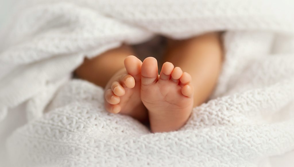 Adorable baby feet covered in a white blanket, maternity and babyhood concept - Image