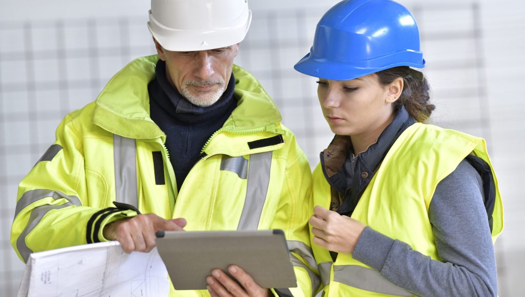 Instructor with apprentice on construction site working with tablet