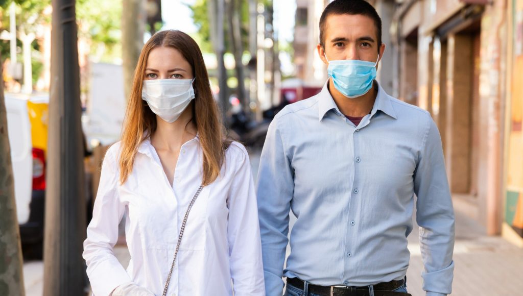 Portrait of adult couple in medical masks and rubber gloves walking along city street. Concept of Covid 19 virus spread prevention and human safety