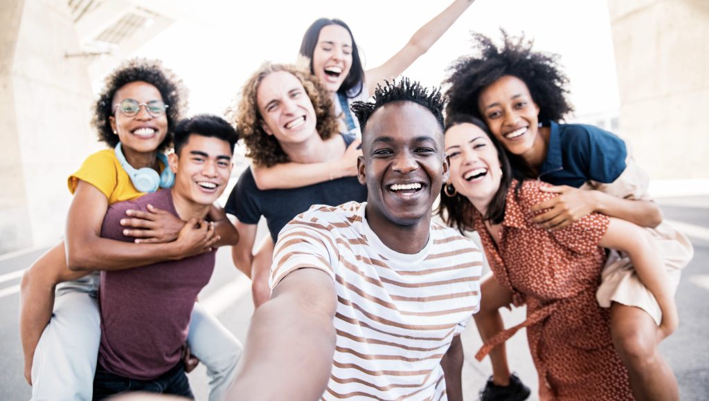 Multicultural happy friends having fun taking group selfie portrait on city street - Young diverse people celebrating laughing together outdoors - Happy lifestyle concept